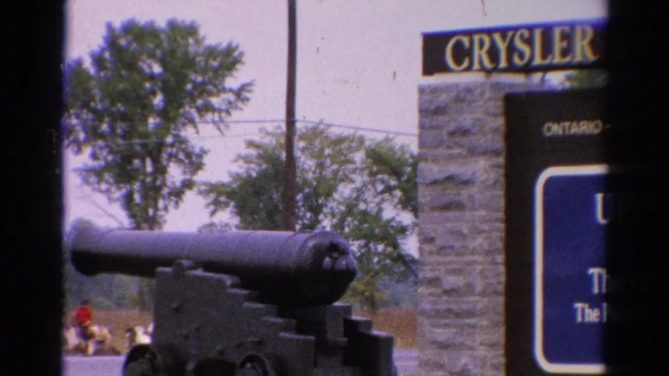 1962 Catskill-area 8mm frame showing a cannon display near a stone sign marked Cryslers Ontario, with trees and a distant visitor visible.