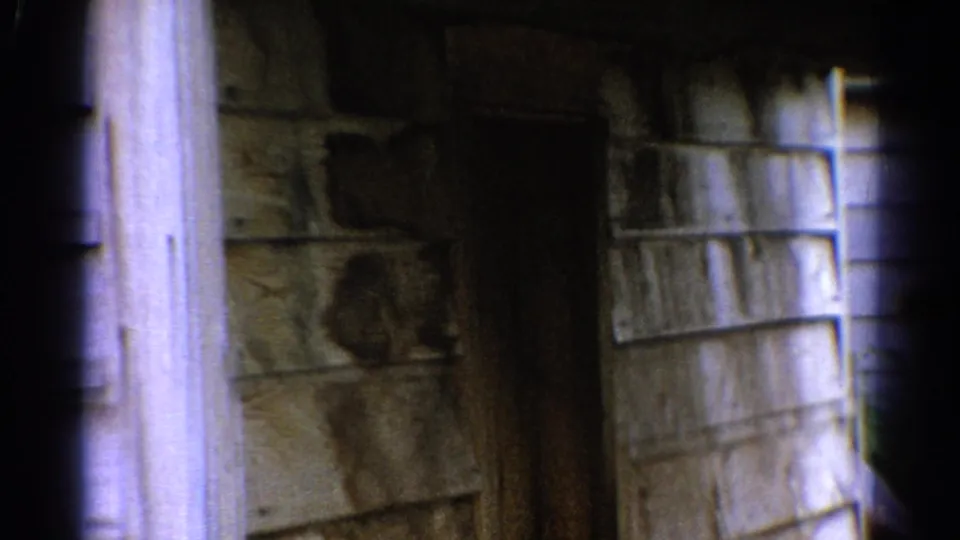 1962 Catskill, New York home-movie frame showing worn wood siding, rough stonework, and dark foreground framing near a house exterior.