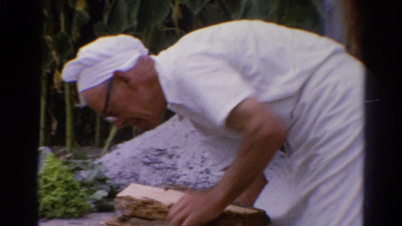 Man in white cap bends lower beside stacked wood outdoors.