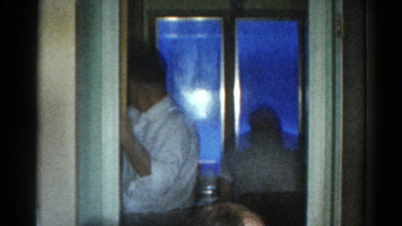 Man in a light shirt seated near a window with blue night outside.