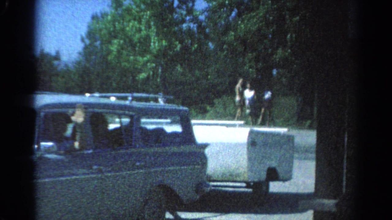 The station wagon and trailer continue past a wooded Catskill roadside, with people visible beyond the low wall.