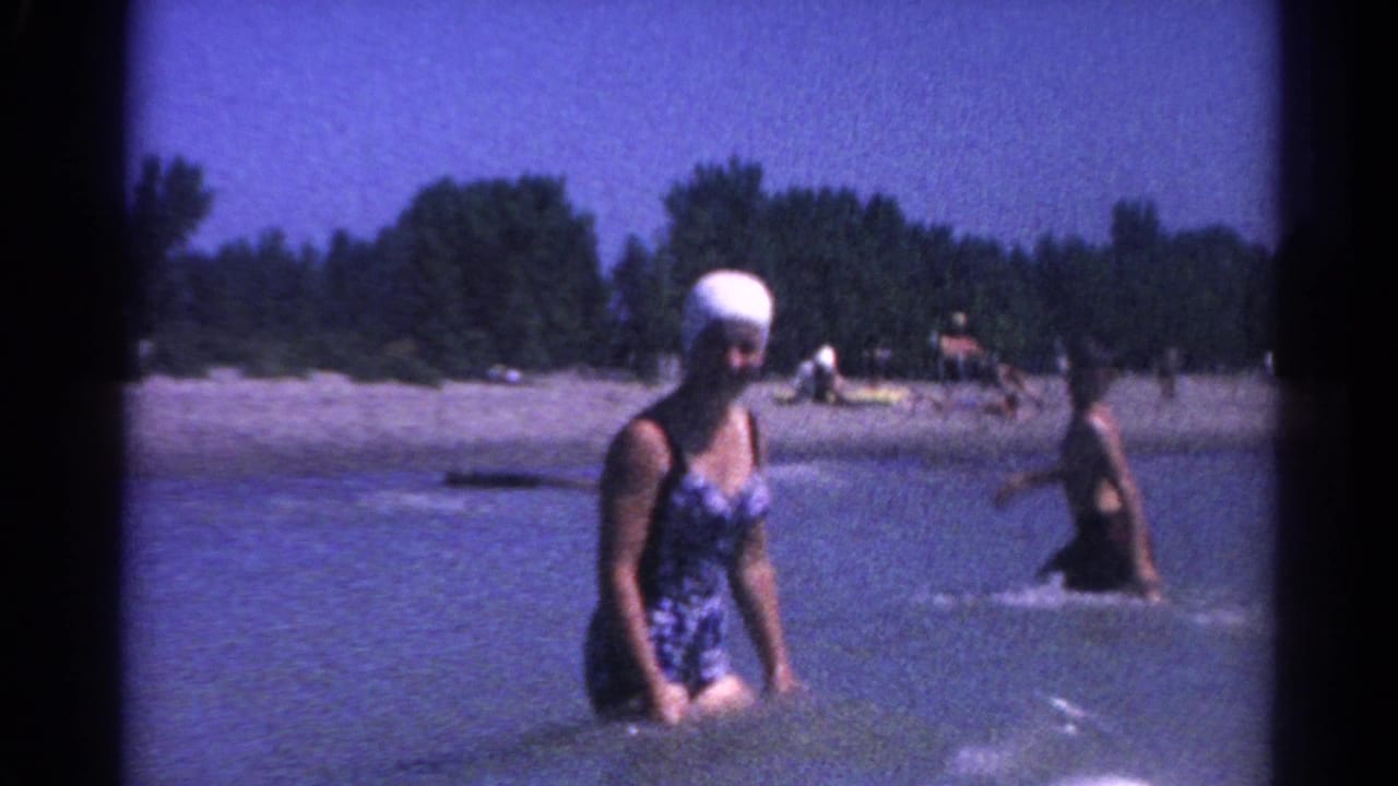 Woman in swim cap wades through lake water while another swimmer splashes nearby.