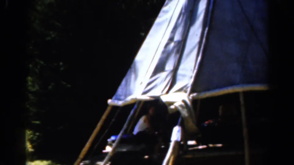 1962 Catskill, New York home-movie frame showing a canvas tent in woods with people seated in shadow inside.