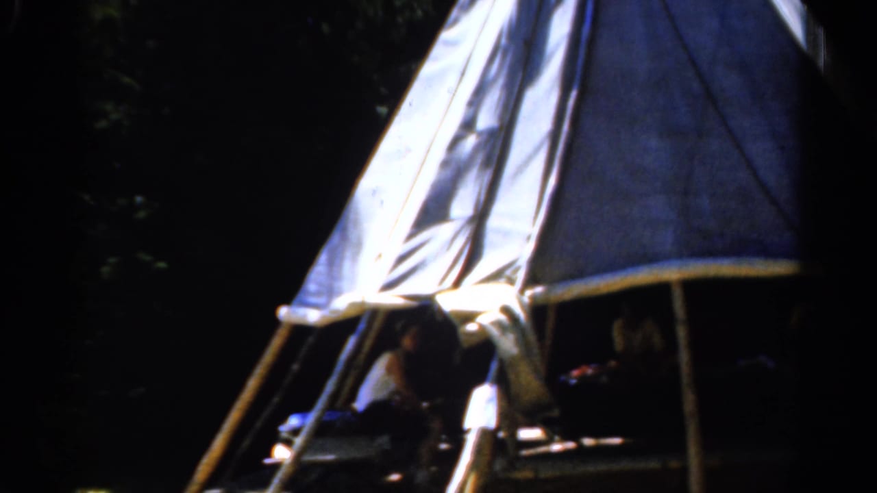 1962 Catskill, New York camping frame with bright tent panels, wooded shade, and several people partly visible inside.
