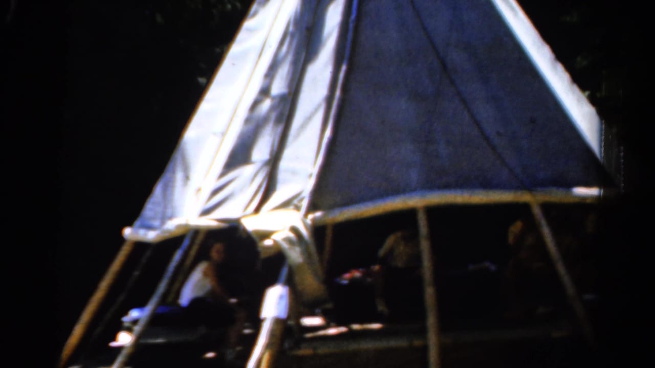 Canvas teepee-like shelter in a forest with people visible in the shaded opening.
