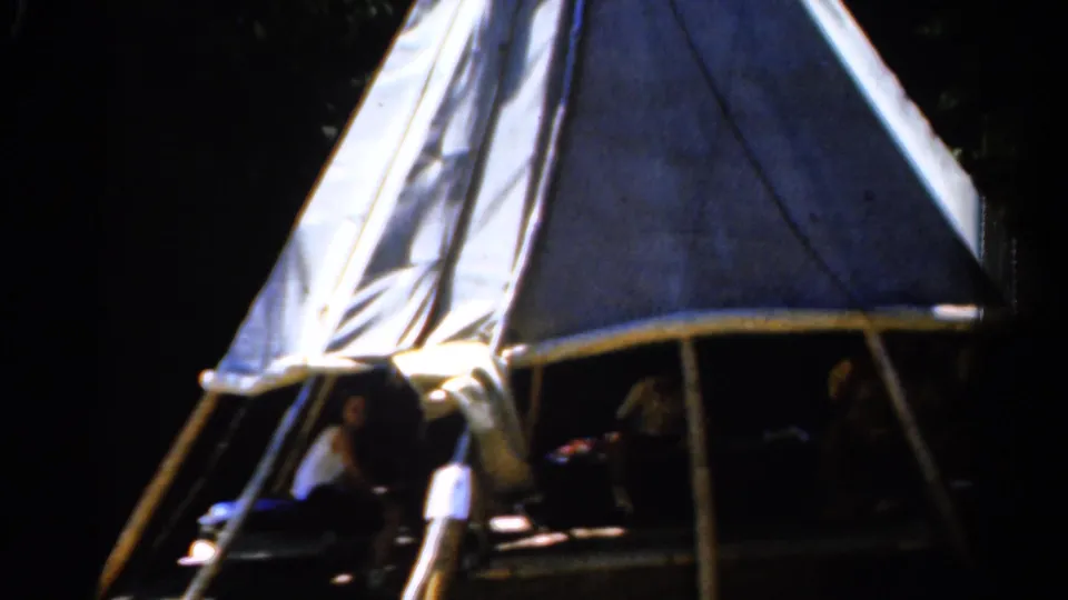 1962 Catskill home-movie frame showing a canvas teepee-like shelter among trees, with people partly visible inside the dark entrance.