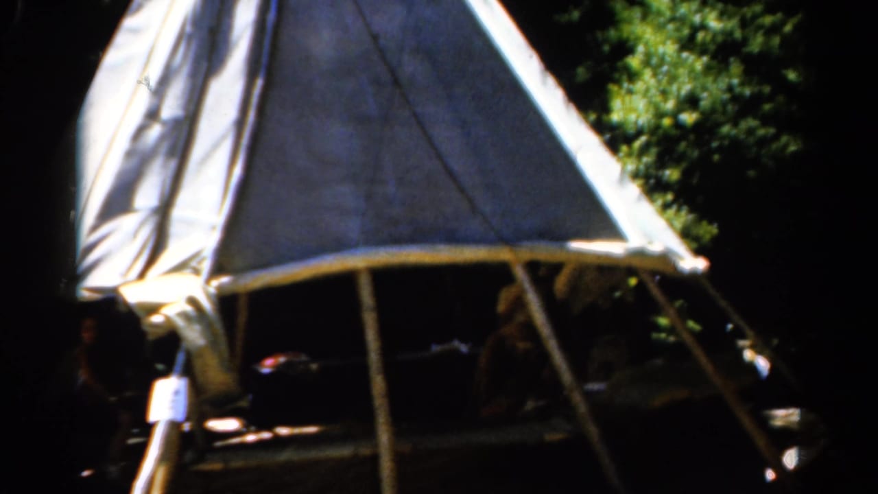 Tent entrance and shaded figures beneath a pale canvas roof.