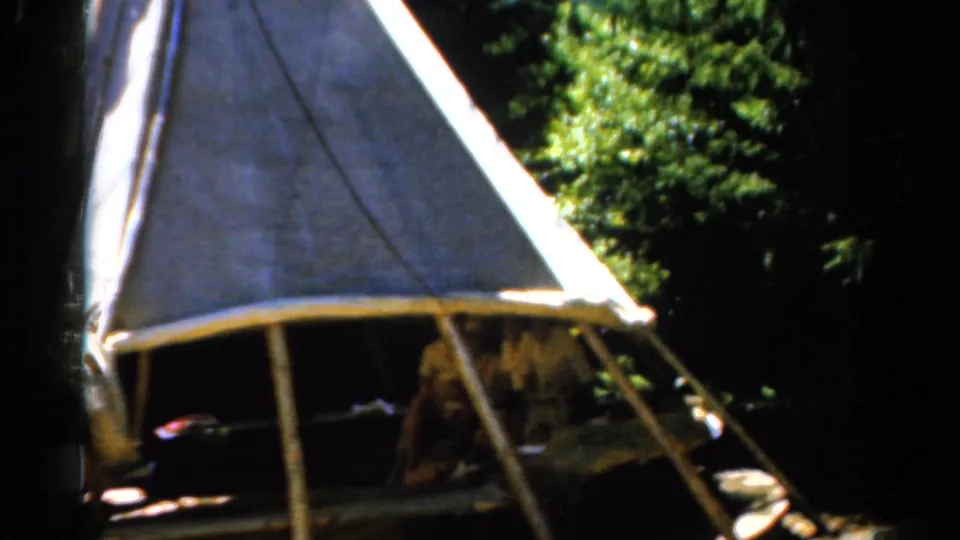 1962 Catskill camping frame showing wooden tent poles, a pale canvas wall, and seated figures partially hidden by shade.
