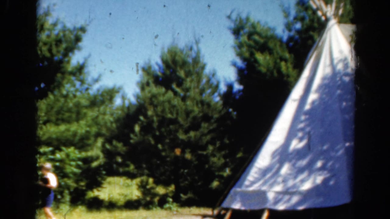 1962 Catskill home-movie frame showing a white teepee-style tent among trees, with a partial person at the left edge.