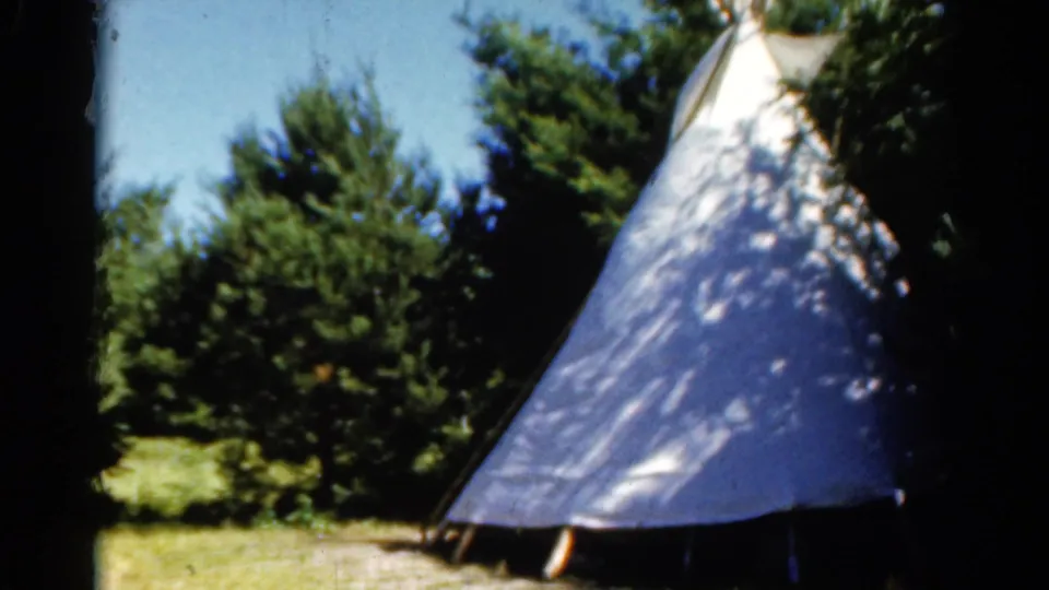 1962 Catskill frame showing a close view of a white teepee-style tent in a wooded camping area.