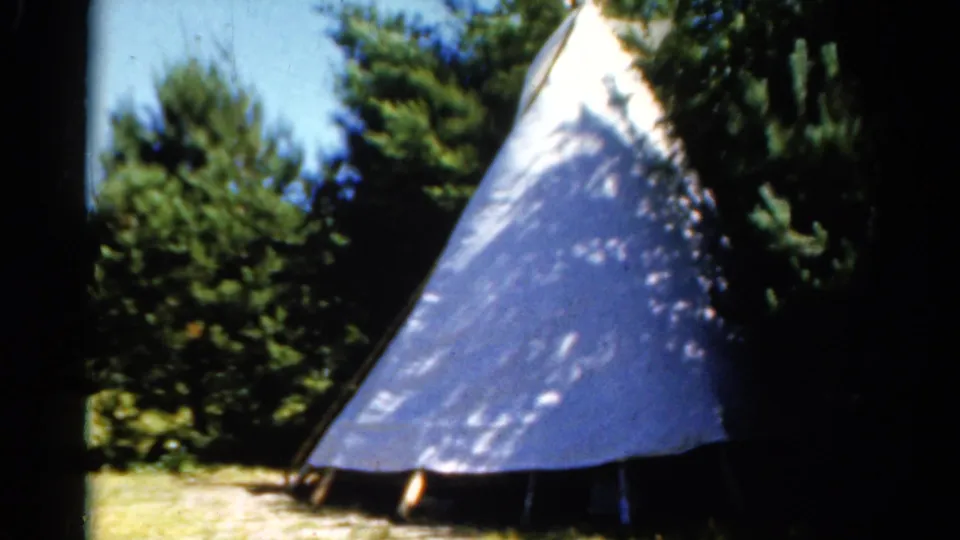 1962 Catskill home-movie frame with a close view of the white teepee-style tent and surrounding forest shade.