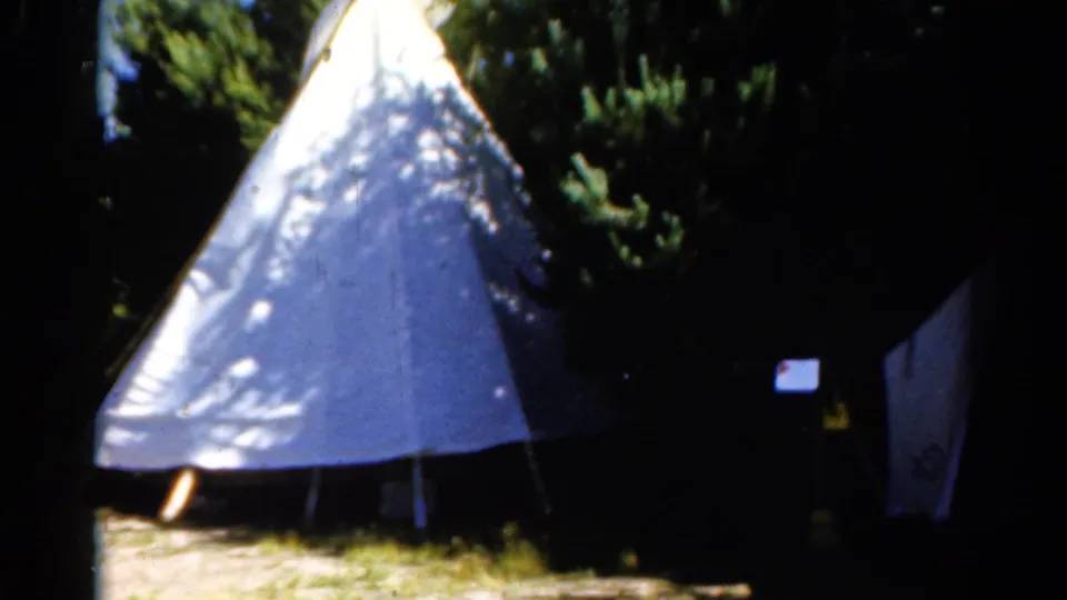 1962 Catskill home-movie frame showing the teepee-style shelter closer in view, with a second canvas tent or panel partly visible to the right.