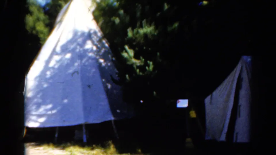 1962 Catskill 8mm frame showing a teepee-style shelter at left and a second canvas tent or panel in shadow at right.