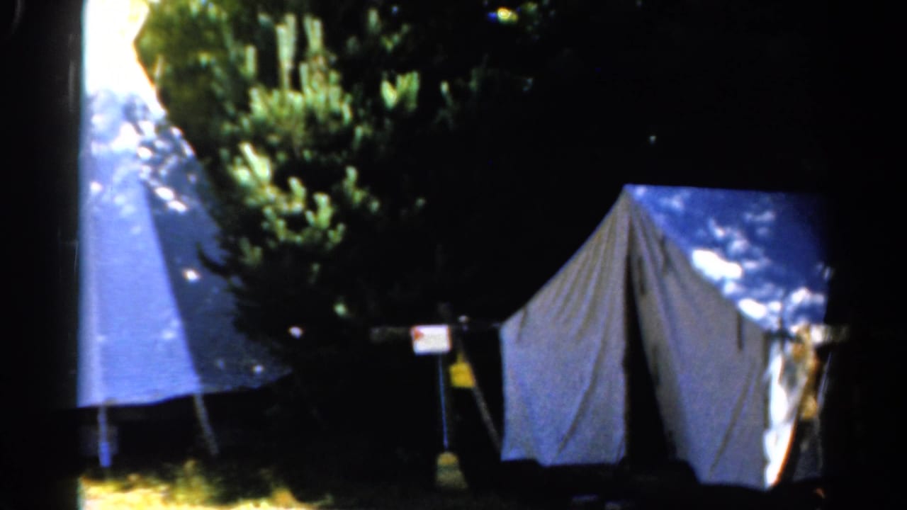 Catskill camping view on 8mm film with two light tents, a small sign or marker, and heavy tree shade.
