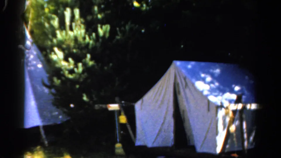 1962 Catskill campsite frame with a large pale tent in the foreground and another tent partly cropped at left.
