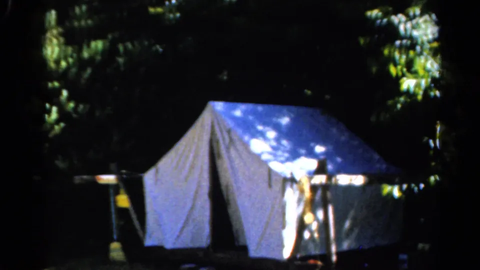 Final 8mm frame of the Catskill campsite, showing a pale tent under trees with another tent cropped along the left edge.