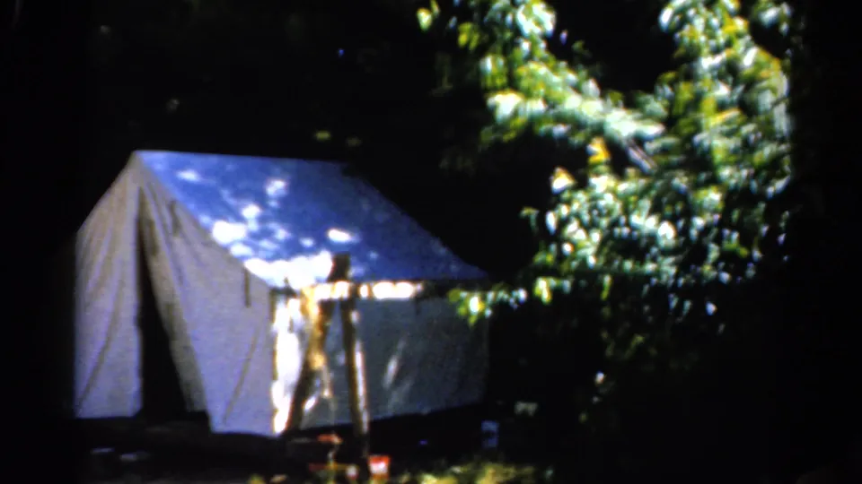 A white tent in the Catskill woods, with a partially visible person standing near the entrance in dappled light.
