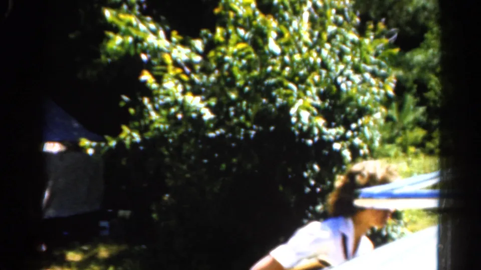 A woman in a brimmed hat and white shirt appears beside dense Catskill foliage, with a white tent partly visible behind her.