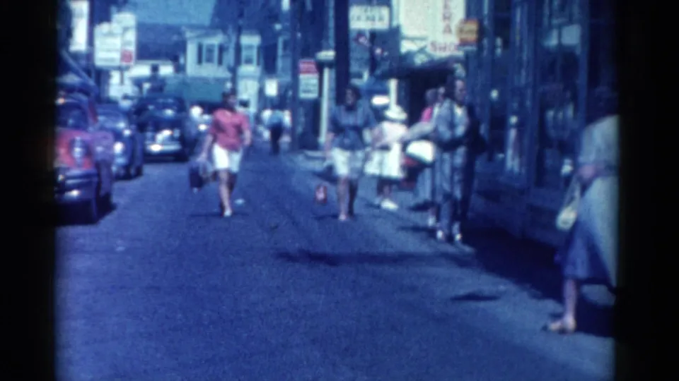 1962 Catskill street footage showing pedestrians approaching the camera near parked cars, shopfronts, and mid-century signage.