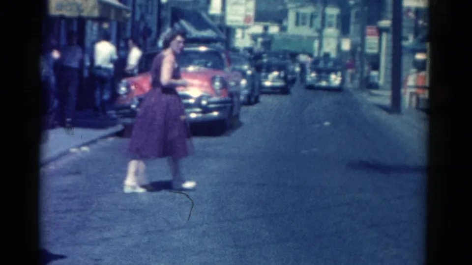 Catskill, New York, 1962 street frame showing a woman crossing the road near parked early 1960s cars and storefronts.