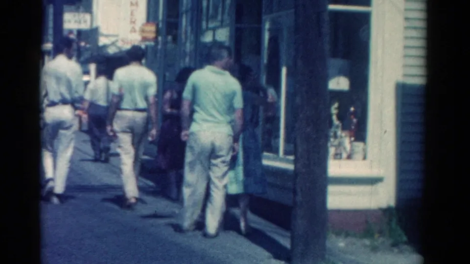 Catskill, New York 1962 sidewalk frame showing pedestrians, retail windows, and a sunlit downtown street edge.