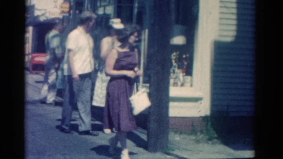 On a Catskill sidewalk, the woman with a white purse moves past storefronts while pedestrians continue behind her.