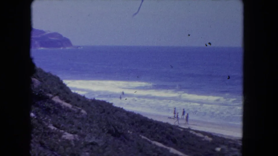 Elevated 1962 Los Angeles-area shoreline view with distant people walking near white surf.