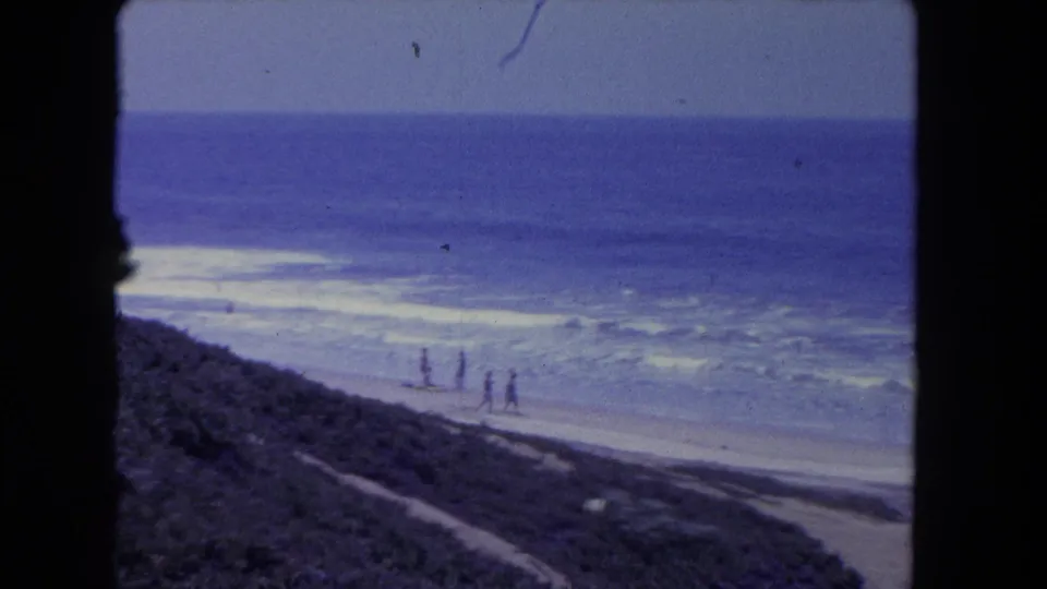 1962 Los Angeles-area beach cutaway with distant figures by the water and a dark grassy hillside foreground.
