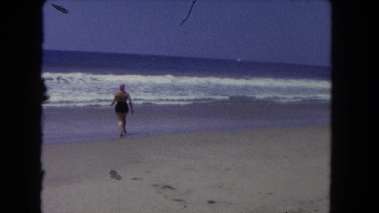 Woman in a dark swimsuit and pink swim cap running across sand toward the ocean.