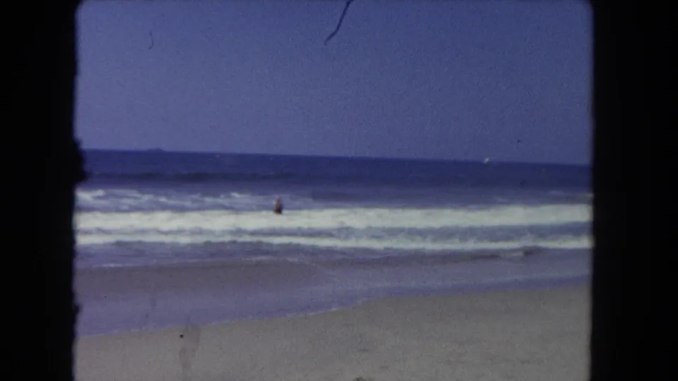A 1962 8mm beach view from Los Angeles shows rolling surf, open water, and a distant person standing or wading offshore.
