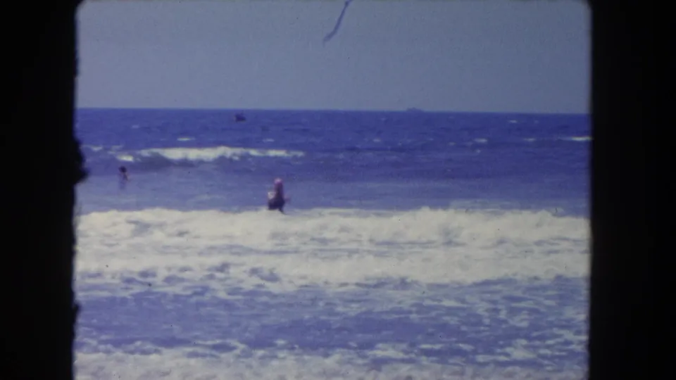 1962 Los Angeles-area beach footage showing a distant swimmer wading in choppy surf beneath a clear horizon.