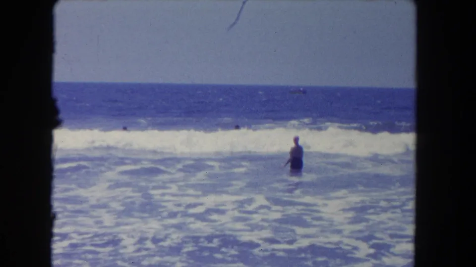 Two distant swimmers are visible in churning surf in 1962 Los Angeles-area beach home-movie footage.