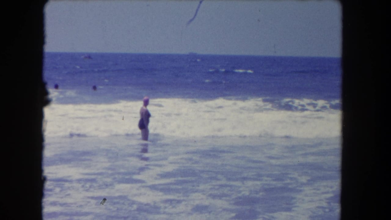 Los Angeles-area 8mm frame from 1962 with a swimmer in a pink cap standing in the surf while other bathers appear farther out.