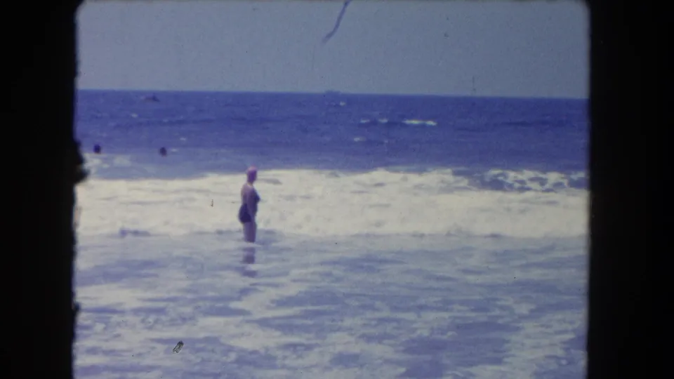 Los Angeles-area 8mm frame from 1962 with a swimmer in a pink cap standing in the surf while other bathers appear farther out.