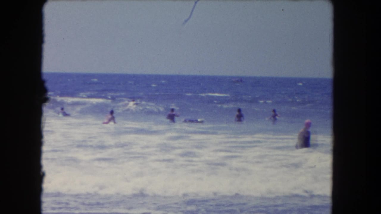 1962 Los Angeles beach footage shows several people in choppy ocean water, with soft focus, faded color, and dark film-gate edges.