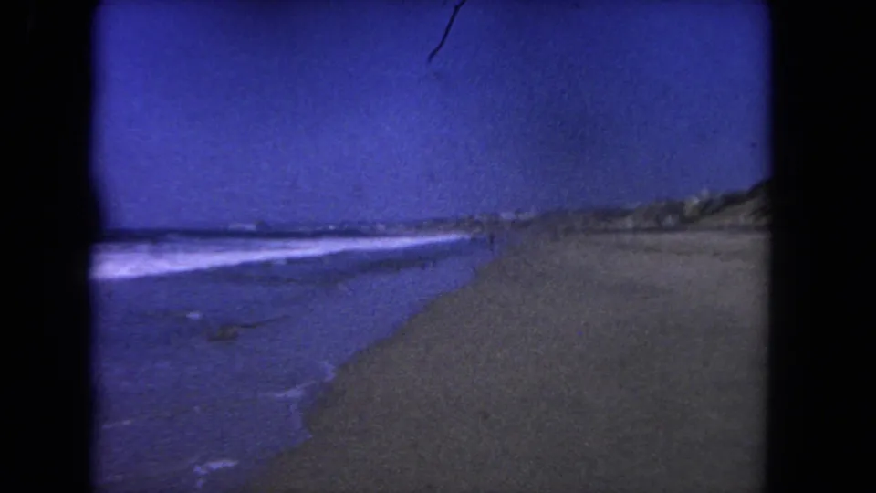 1962 Los Angeles-area shoreline frame showing waves rolling along wet sand with dunes receding in the distance.