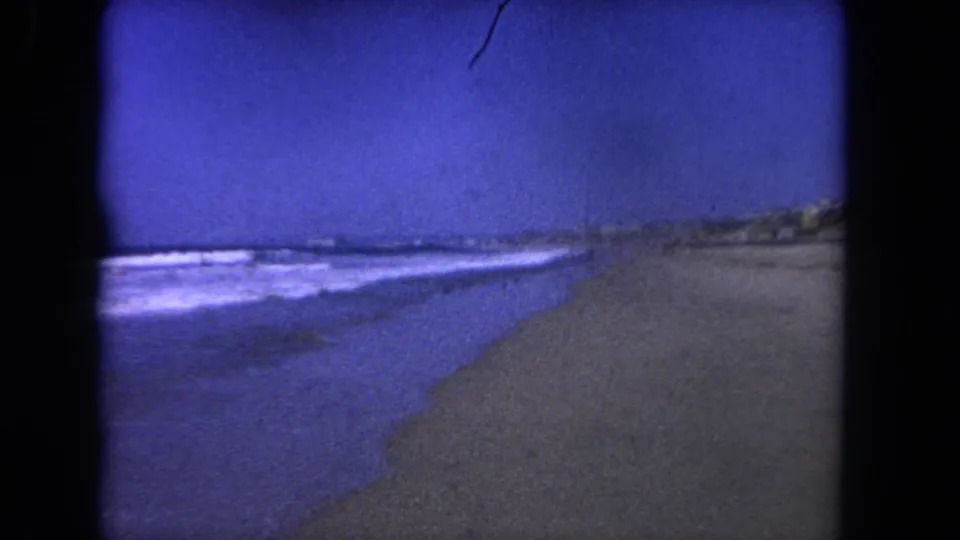 Blue-toned 1962 Los Angeles shoreline view with small waves, open beach, and distant coastal dunes.