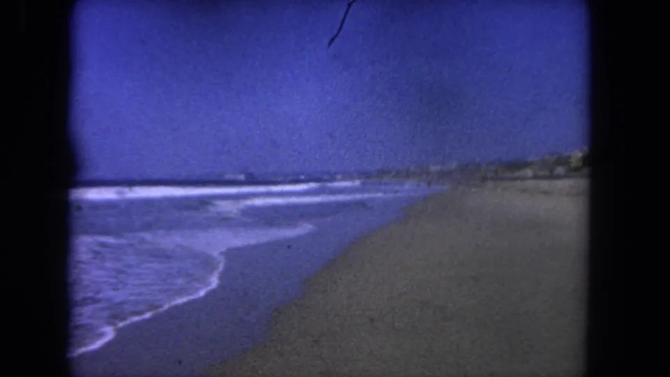 8mm Los Angeles beach frame showing foamy surf curling onto wet sand beneath a clear blue sky.