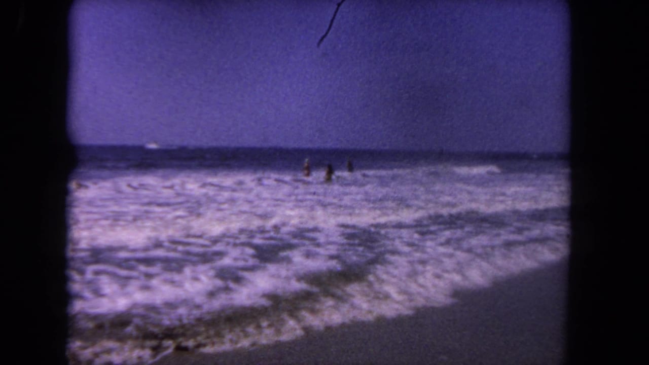 Distant beachgoers stand in foamy surf with waves rolling toward the sand.