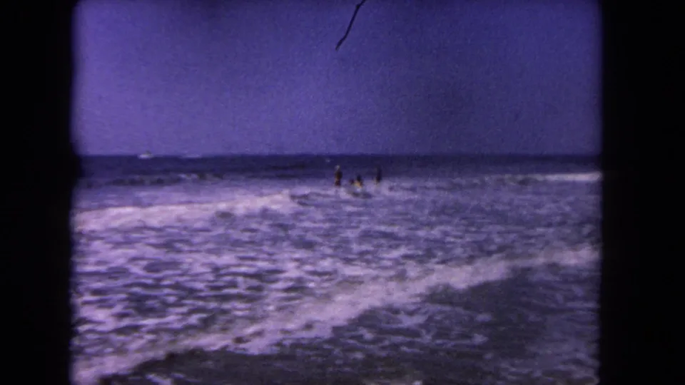 8mm home-movie view of Los Angeles beachgoers in the surf with a wide band of foamy water in front.