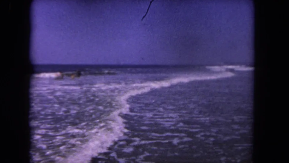 1962 Los Angeles-area 8mm view of ocean surf curving toward shore, with small distant figures near the waterline.
