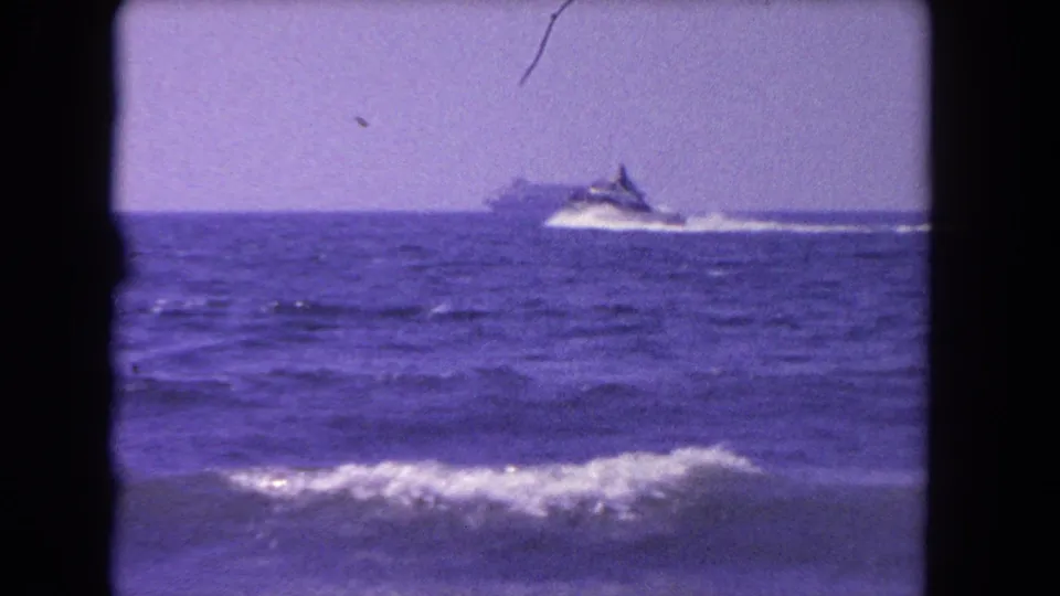 1962 Los Angeles-area 8mm frame showing a distant speedboat moving across open water beyond low foreground waves.