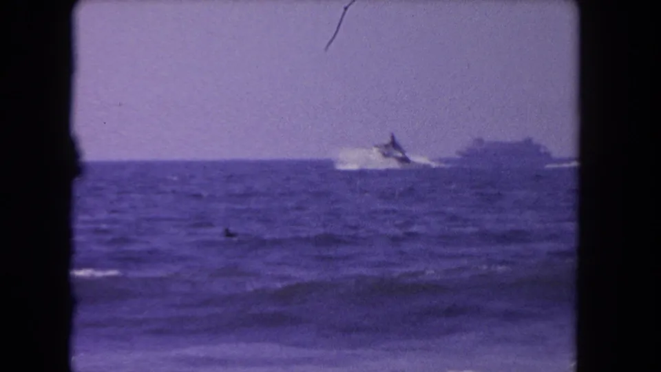 1962 Los Angeles-area coastal frame with a speedboat offshore, a faint distant vessel shape, and a small swimmer or person in the water.