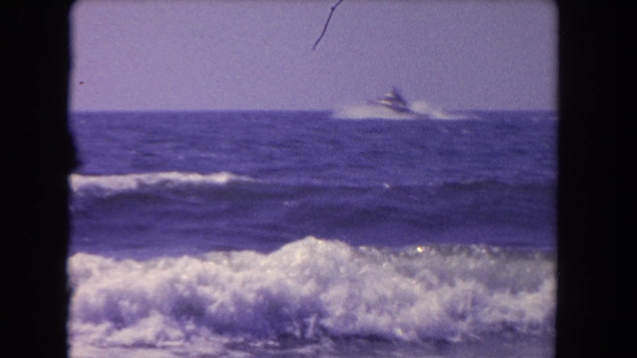 1962 Los Angeles-area coastal view with breaking surf and a distant small motorboat on blue water.