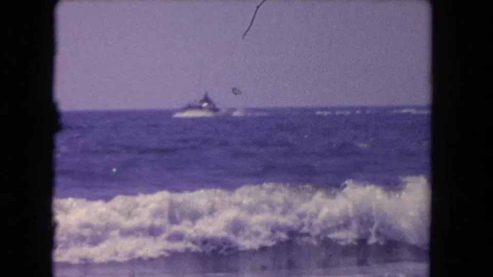 1962 Los Angeles-area ocean view with foamy surf in front and a small boat near the horizon.