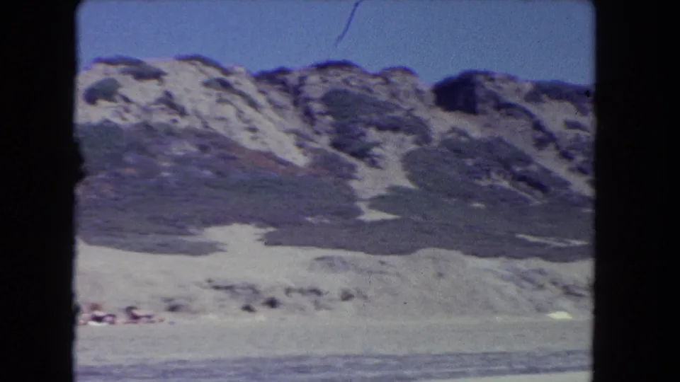 1962 Los Angeles-area 8mm frame showing a pale ridge with dark scrub patches and a flat foreground below.