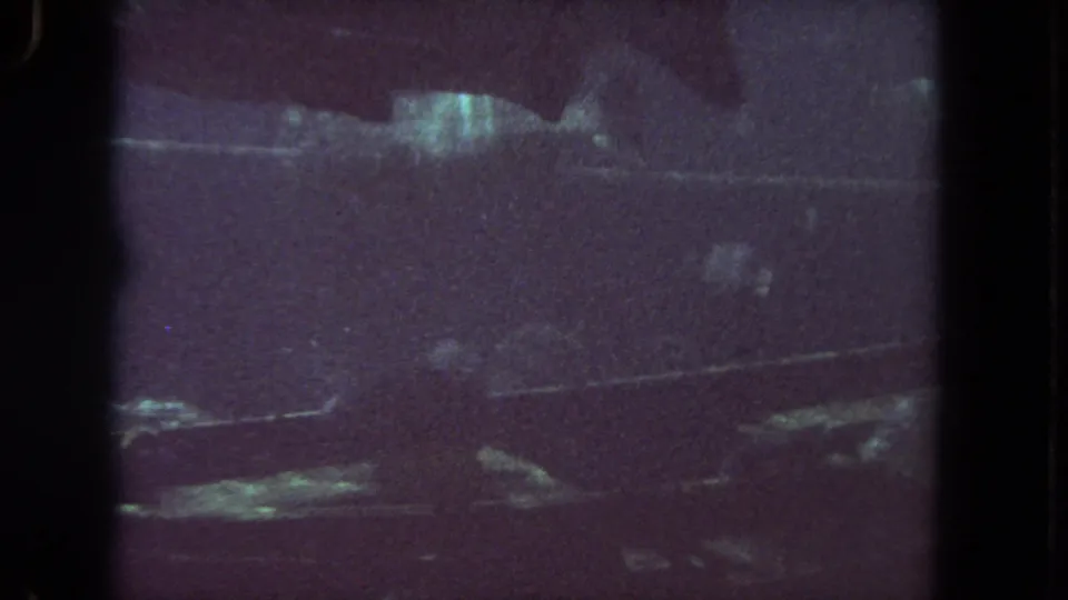 Soft 8mm frame showing a fish shape inside the aquarium, with horizontal reflections and a purple-tinted home-movie look.