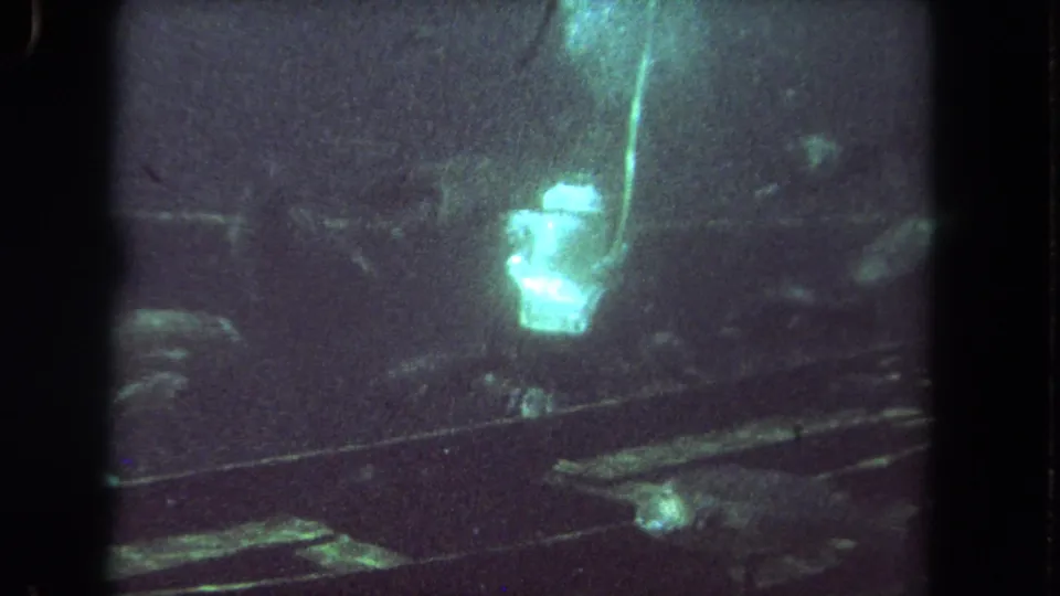 1962 Los Angeles 8mm frame showing the diver more frontally in a dim aquarium tank, with bubbles rising and fish forms below.