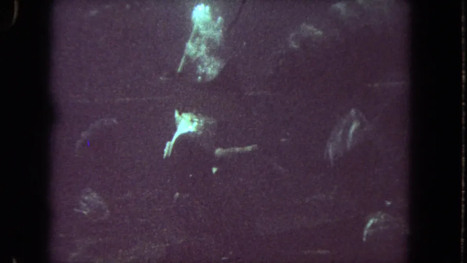 The diver appears partially obscured in murky underwater 8mm footage, with bubbles and green highlights against a dark background.