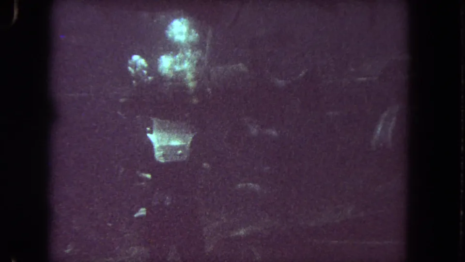 The scuba diver is more centered here, surrounded by bubbles in grainy, low-light 8mm underwater footage from the Los Angeles clip.